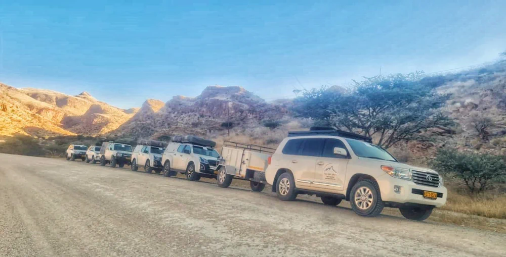 Der Fuhrpark von Dusty Trails Safaris bei einer größeren Gruppenreise vor einer Berglandschaft - Namibia